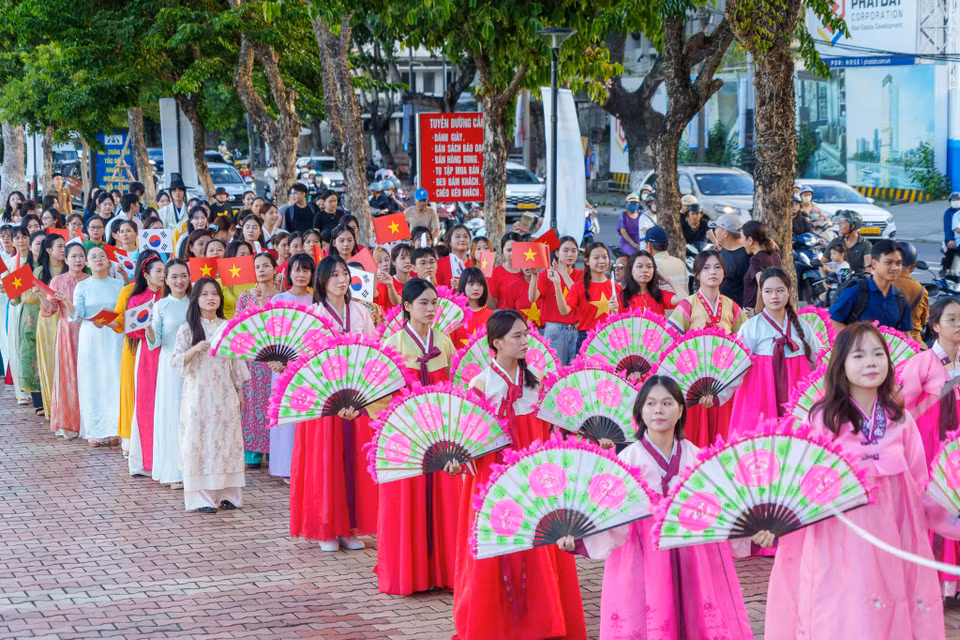 Ngay sau đoàn múa quạt là đoàn diễu hành mặc Áo dài Việt Nam cầm cờ hai nước vẫy chào, thể hiện tình hữu nghị bền chặt. (Ảnh: Thanh Phong/Vietnam+)