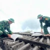 Các chiến sỹ giúp người dân đưa bao cát lên mái nhà để tránh tốc mái tôn khi gió bão. (Ảnh: TTXVN phát)