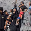 Người dân Palestine đứng trên đống đổ nát sau các cuộc không kích của Israel xuống Dải Gaza. (Ảnh: IRNA/TTXVN)