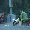 Nhiều người đi xe máy phải xuống dắt bộ vì mưa quá lớn. (Ảnh: Hoàng Hiếu/TTXVN)