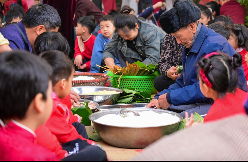 Học sinh Trường Tiểu học Dương Liễu B (Hà Nội) gói trải nghiệm gói bánh chưng ngày Tết dưới sự hướng dẫn của người lớn. (Ảnh: NTCC)