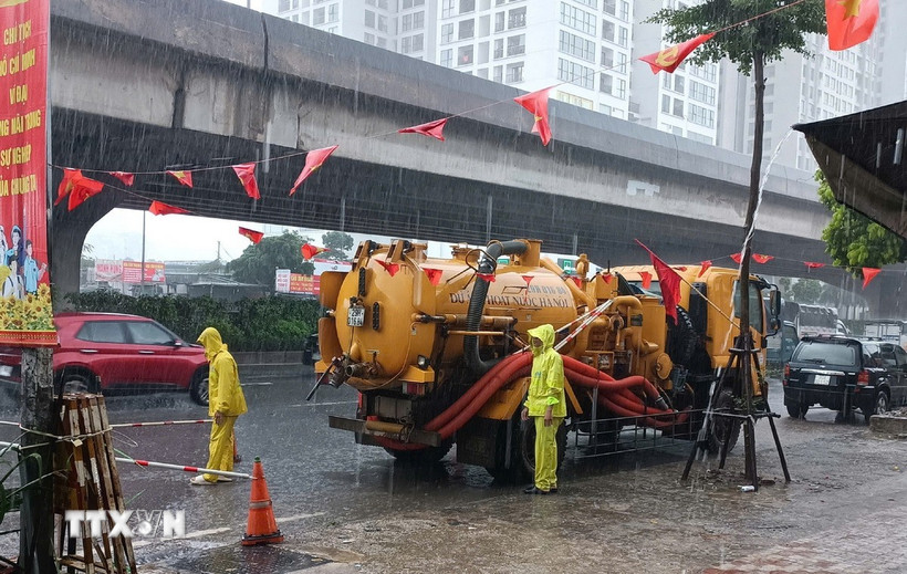 Công nhân ứng trực tiêu thoát nước trong mưa lớn tại đường Nguyễn Xiển. (Ảnh: Nguyễn Thắng/TTXVN)