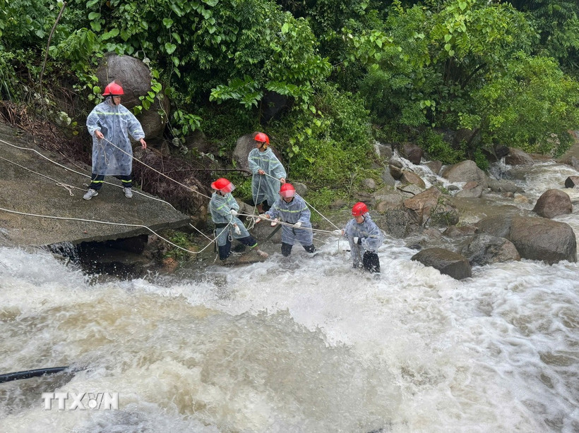 Lực lượng chức năng căng dây để trục vớt thi thể người đàn ông dưới dòng nước chảy siết. (Ảnh: TTXVN phát)