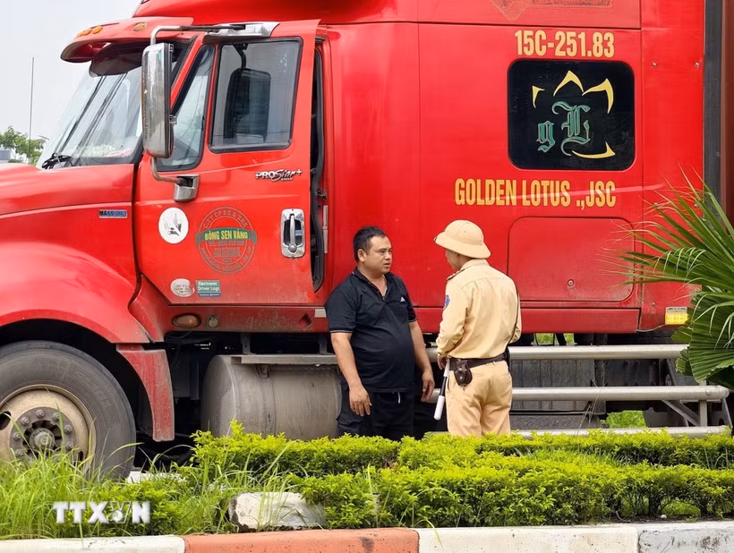 Cán bộ Đội Cảnh sát giao thông đường bộ số 15 (Phòng Cảnh sát giao thông Hà Nội) tuyên truyền, hướng dẫn lái xe chấp hành quy định về tải trọng và lộ trình lưu thông đối với phương tiện ra, vào khu công nghiệp Nguyên Khê. (Ảnh: Trung Nguyên/TTXVN)