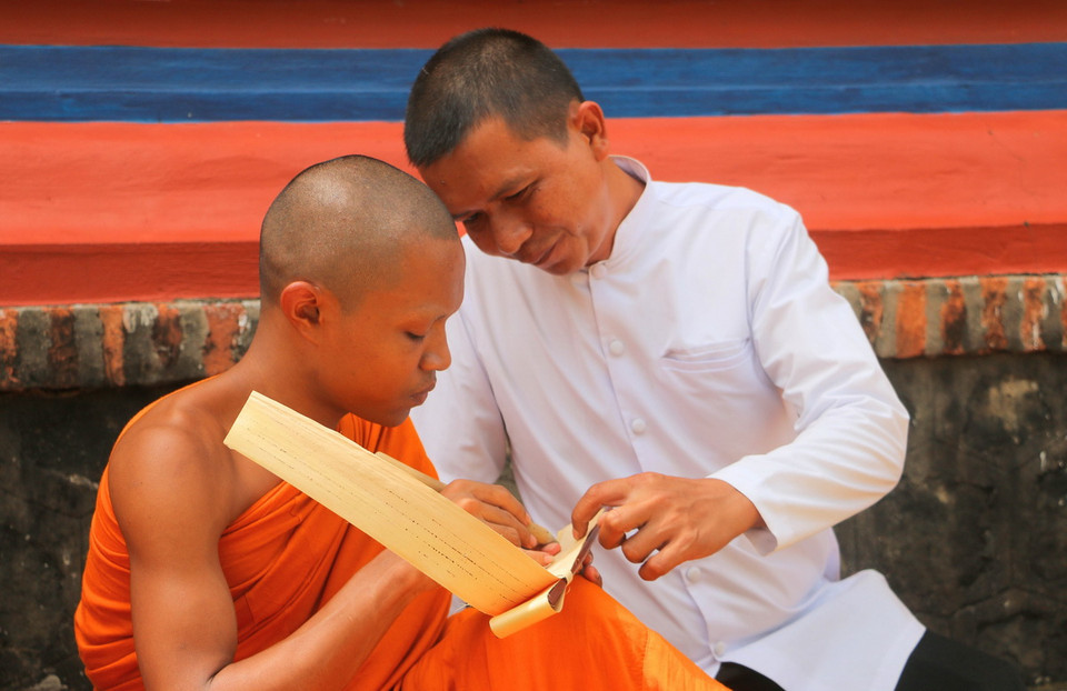 Anh Ry Thy (áo trắng) - người đang theo học cách viết kinh lá buông từ Trưởng lão Hòa thượng Chau Ty nhiều năm đang hướng dẫn các sư tại chùa Sà Lôn (xã Lương Phi, huyện Tri Tôn, An Giang) kỹ thuật viết chữ Pali trên lá buông. (Ảnh: Công Mạo/TTXVN)