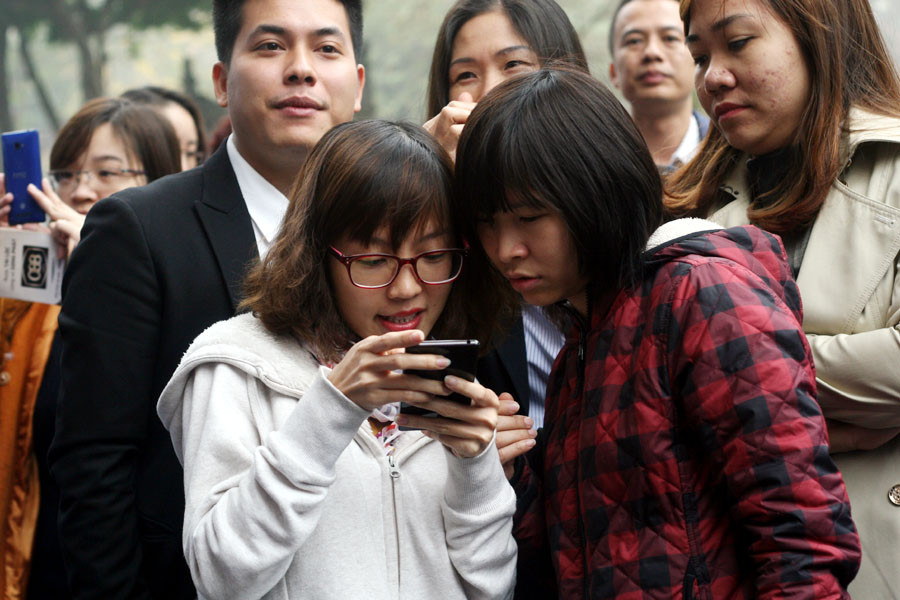 Tranh thủ dùng smartphone lúc xếp hàng chờ đợi. (Ảnh: T.H/Vietnam+)