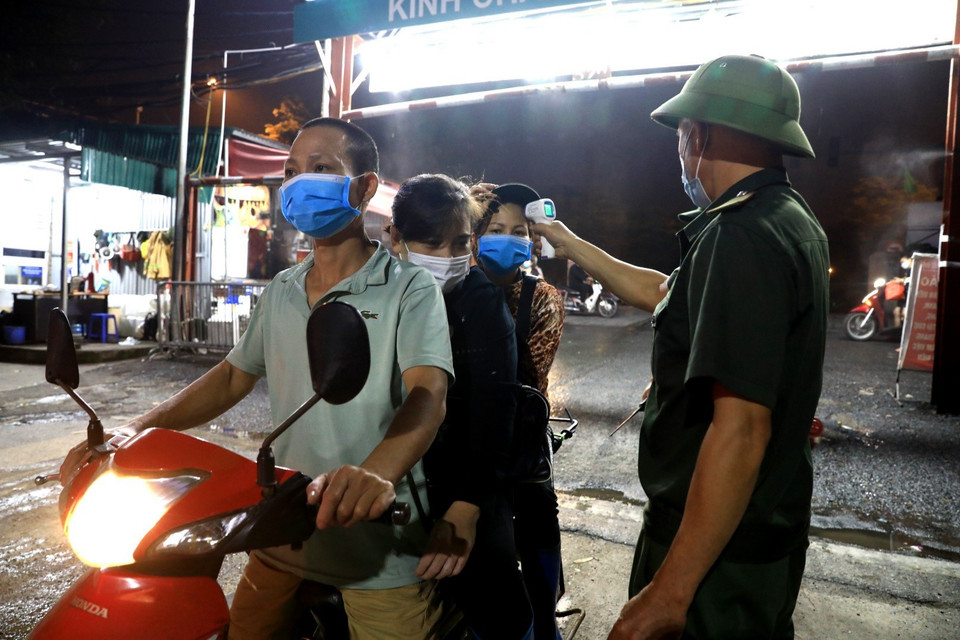 Nhân viên Ban quản lý chợ Long Biên kiểm tra thân nhiệt cho các tiểu thương mỗi khi ra vào. (Ảnh: Thành Đạt/TTXVN)