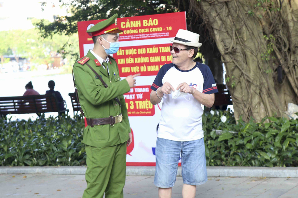 Lực lượng chức năng nhắc nhở người dân tại khu vực hồ Hoàn Kiếm đeo khẩu trang. (Ảnh: Tuấn Đức/TTXVN)