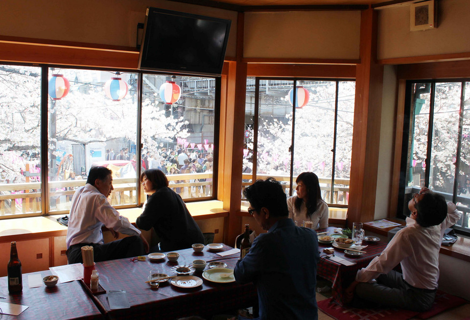 Người dân dùng cơm tại một quán ăn ven sông Meguro và tranh thủ ngắm hoa anh đào qua khung cửa tầng 2.