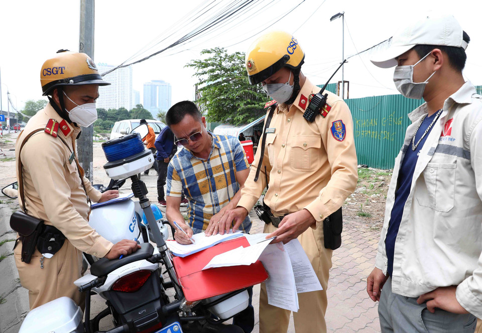 Cán bộ Đội cảnh sát giao thông số 6 lập biên bản xử lý tài xế xe khách với lỗi dừng đỗ, đón trả khách sai quy định tại tuyến đường Phạm Hùng. (Ảnh: Phạm Kiên/TTXVN)