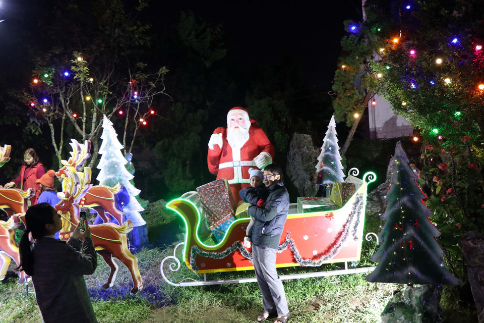 Người dân chụp ảnh bên tiểu cảnh ông già Noel tại nhà thờ Phủ Cam ở thành phố Huế. (Ảnh: Đỗ Trưởng/TTXVN)