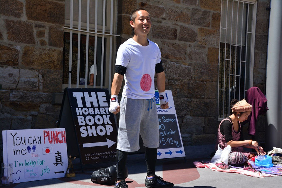 Chàng trai Nhật Bản khiến không ít người đi đường mỉm cười vì dòng chữ quảng cáo biểu diễn : "Bạn có thể đấm tôi. Tôi đang tìm việc." (Ảnh: Võ Giang/Vietnam+)