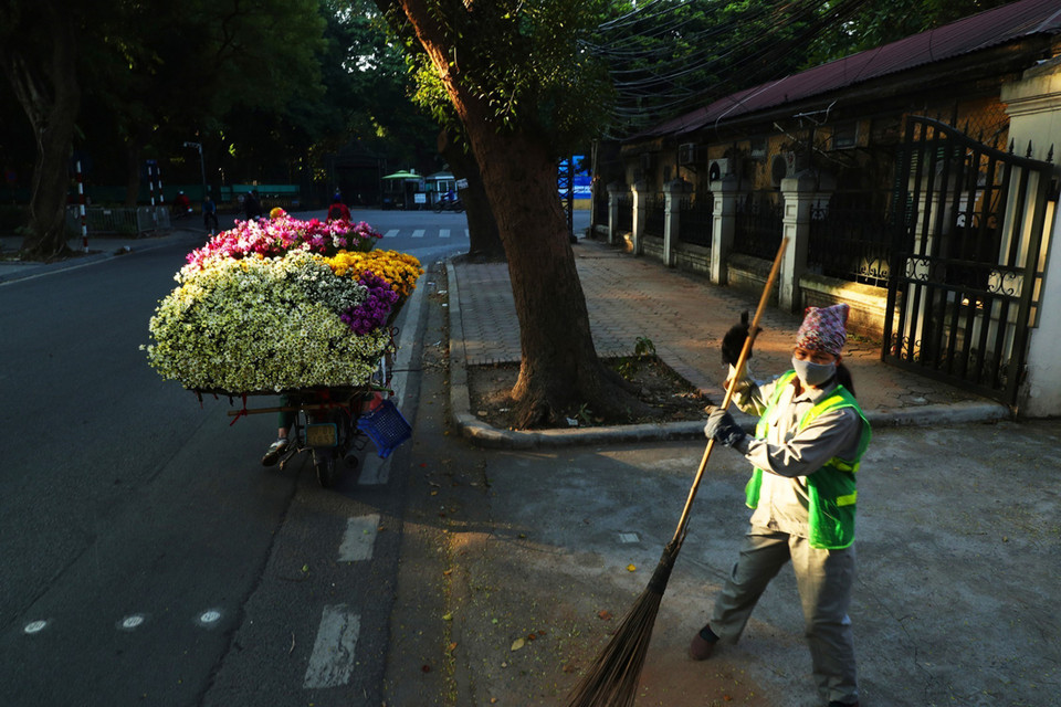 Một người lao công quét đường, bên một sạp hoa trong ánh nắng sớm trên phố Mai Xuân Thưởng. (Ảnh: Lâm Khánh/TTXVN)