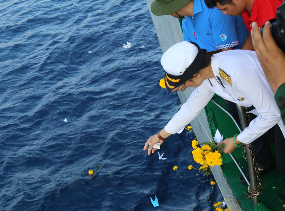 Thượng úy Hải quân Trần Thị Thủy (con gái liệt sỹ, Anh Hùng lực lượng vũ trang Trần Văn Phương hy sinh trên quần đảo Trường Sa) thả những cánh hoa tươi thắm từ tàu Trường Sa 571 xuống biển để tưởng niệm các liệt sỹ. (Ảnh: Sỹ Tuyên/TTXVN) 