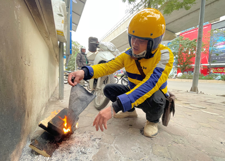 Tài xế công nghệ đang ngồi đốt củi sưởi ấm trong lúc chờ khách. (Ảnh: Minh Hiếu/Vietnam+) 