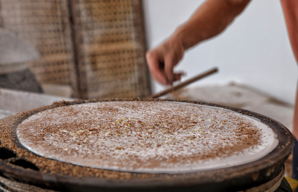 Vừng và lạc sống đã giã dập được rắc lên bánh trong khi tráng. (Ảnh: Danh Lam/TTXVN)