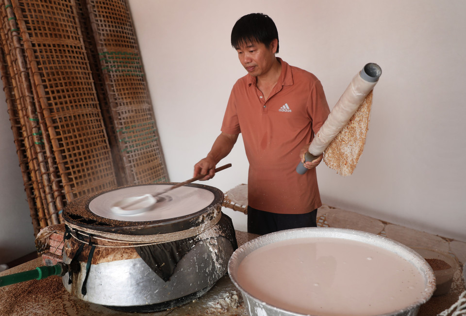 Khi bánh đã được tráng chín, người ta khéo léo dùng một ống to, dài quấn lớp bánh quanh ống lấy ra khỏi nồi hơi để mang trải đều trên phên. (Ảnh: Danh Lam/TTXVN)