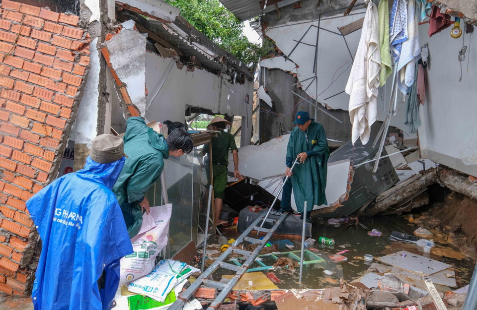 Dân quân, bảo vệ dân phố tìm kiếm tài sản, vật dụng còn lại trong một ngôi nhà bị sạt lở nhấn chìm xuống sông Bình Thủy. (Ảnh: Thanh Liêm/TTXVN)