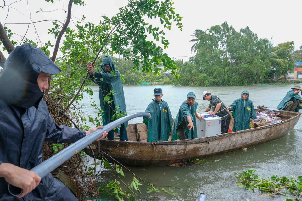 Dân quân, bảo vệ dân phố dùng thuyền hỗ trợ các hộ dân di dời tài sản từ khu vực nhà bị sạt không thể tiếp cận bằng đường bộ. (Ảnh: Thanh Liêm/TTXVN)