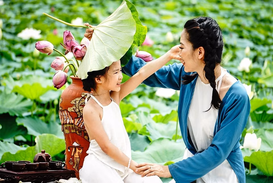 Hai mẹ con bên đầm sen nở sớm ở Hồ Tây (Hà Nội). (Ảnh: Khánh Hòa/TTXVN)