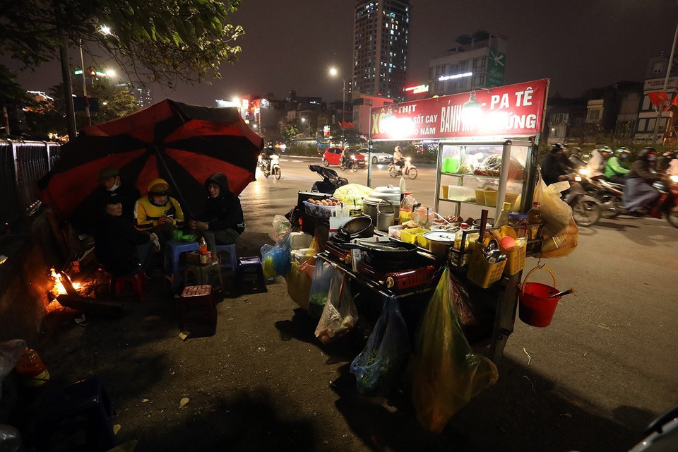 Một quán bán hàng rong phải dùng ô che gió và đốt lửa giữ ấm trong đêm lạnh giá buốt. (Ảnh: Phan Tuấn Anh/TTXVN)