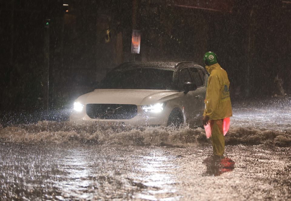 Công nhân Công ty thoát nước Hà Nội có mặt để hướng dẫn người dân khi đi qua điểm ngập ngã tư Phan Bội Châu - Lý Thường Kiệt, quận Hoàn Kiếm. (Ảnh: Hoàng Hiếu/TTXVN)