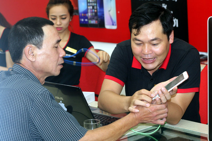 Nhân viên FPT Shop hướng dẫn ông Lương Văn Trương sử dụng iPhone 6S Plus mới mua. (Ảnh: Trung Hiền/Vietnam+)