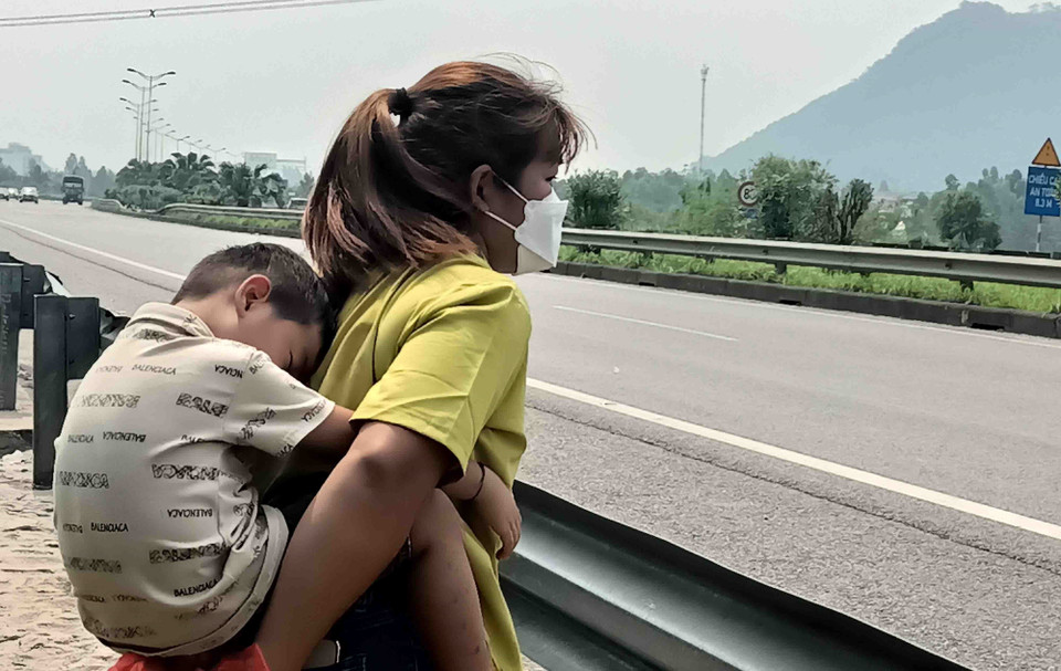 Một hành khách nhí đợi xe cùng mẹ trên tuyến đường có cao tốc đi qua khu vực thị trấn Kim Long, Tam Dương, Vĩnh Phúc.(Ảnh: Hoàng Hùng/TTXVN)