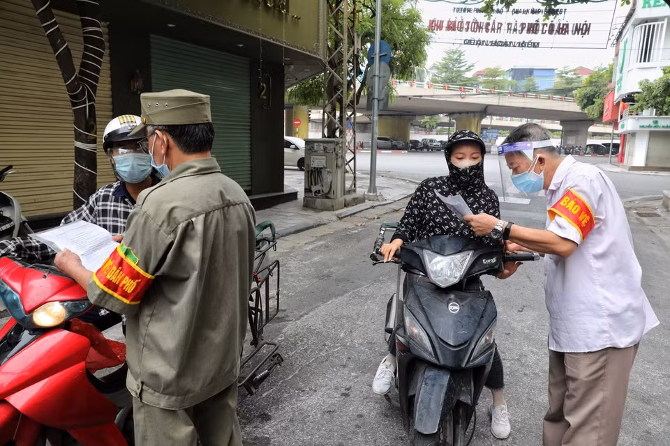 Thành viên Tổ phòng, chống COVID cộng đồng phường Hàng Buồm kiểm tra, nhắc nhở người dân hoàn thiện các mục còn thiếu đối với giấy đi đường theo quy định mới. (Ảnh: Thành Đạt/TTXVN)
