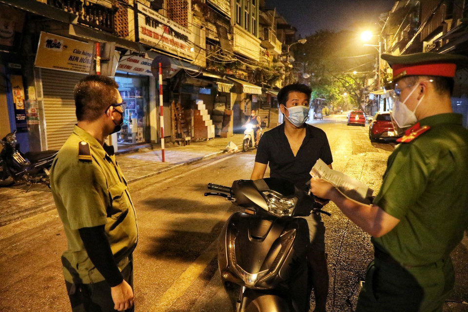 Lực lượng chức năng phường Hàng Buồm kiểm tra giấy đi đường của người dân khi ra khỏi địa bàn (Ảnh chụp lúc 23 giờ). (Ảnh: Thành Đạt/TTXVN)