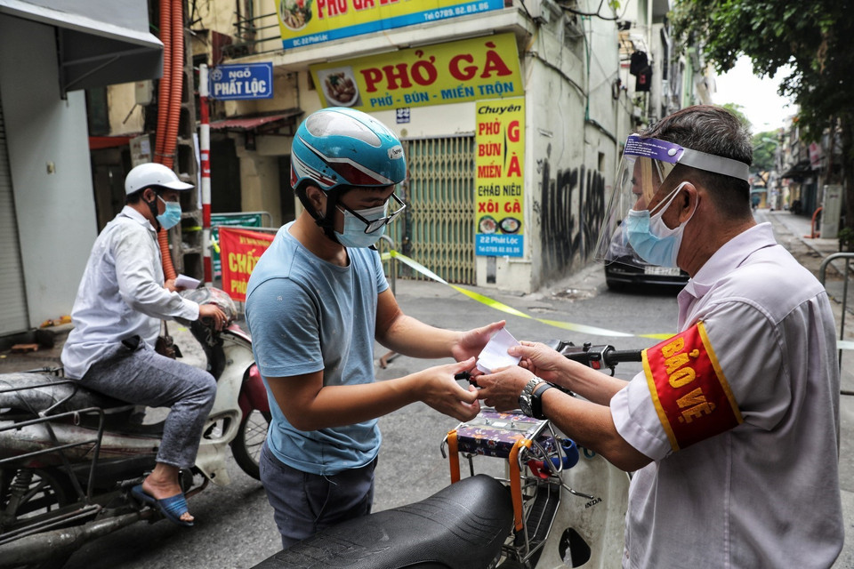 Thành viên Tổ phòng, chống COVID cộng đồng phường Hàng Buồm kiểm tra giấy đi đường theo quy định mới của người dân khi ra vào địa bàn. (Ảnh: Thành Đạt/TTXVN)