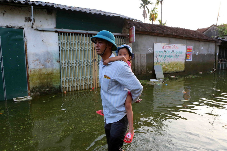 Hằng ngày, người dân xã Nam Phương Tiến phải di chuyển, chung sống trong làn nước và môi trường bị ô nhiễm nghiêm trọng bởi đủ loại chất thải tồn đọng lâu ngày. (Ảnh: Thành Đạt/TTXVN)