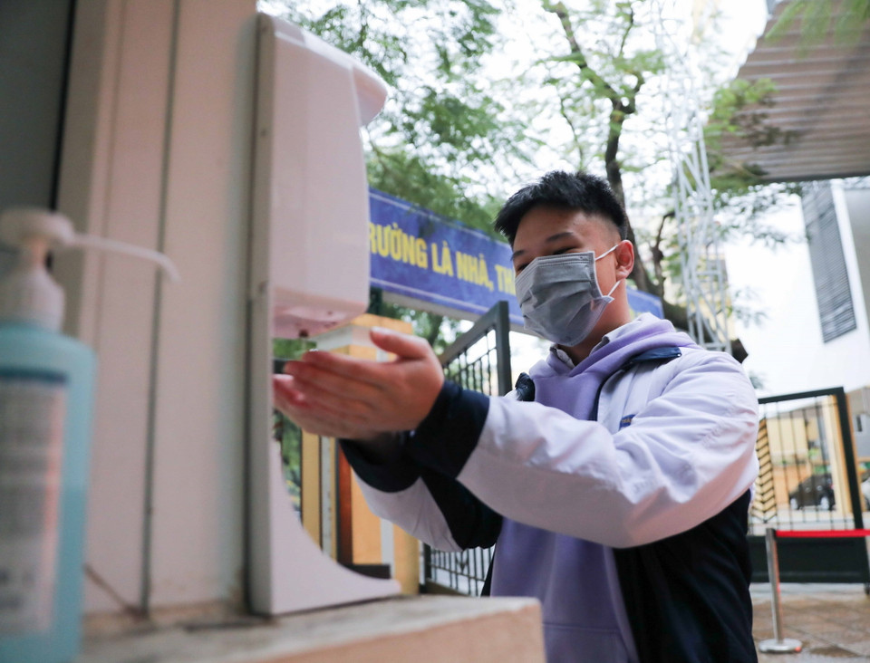 Học sinh lớp 12 trường THPT Trần Nhân Tông (quận Hai Bà Trưng) thực hiện đo thân nhiệt và sát khuẩn tay khi tới trường học trực tiếp từ sáng 10/1. (Ảnh: Thanh Tùng/TTXVN)