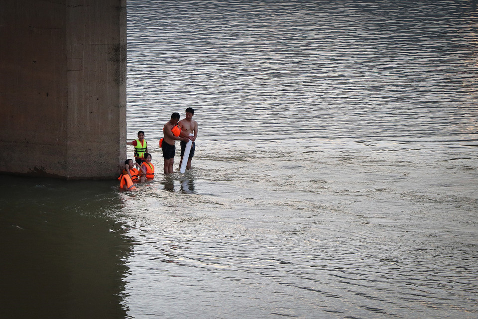 Người lớn lẫn trẻ em xuống tắm sông Đà trong những ngày này khi nước sông đang lên và dòng chảy mạnh, phớt lờ những biển cấm, cảnh báo nguy hiểm. (Ảnh: Trọng Đạt/TTXVN)