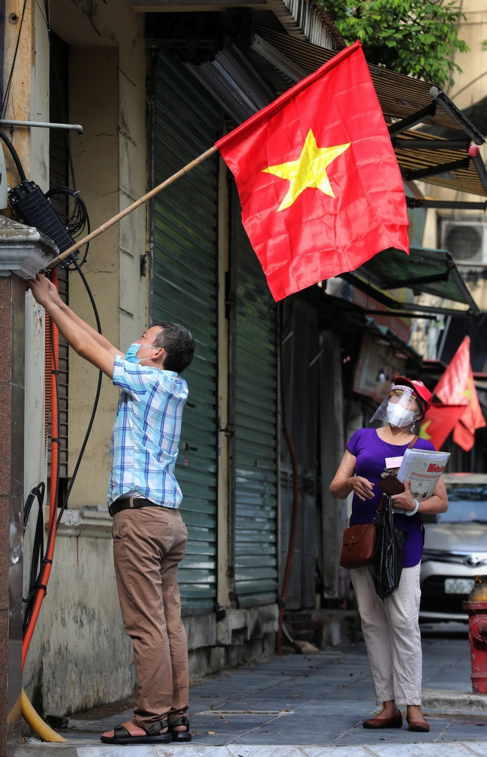 Cán bộ phường Thụy Khuê, quận Ba Đình đi treo cờ Tổ quốc cho các gia đình không thể ra đường, hoặc không có mặt ở nơi cư trú trên địa bàn phường. (Ảnh: Thành Đạt/TTXVN)