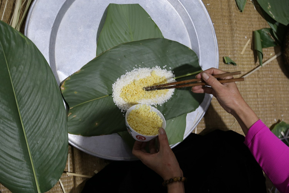  Xếp hai lá dong chồng lên nhau theo chiều dọc, quay mặt xanh của lá vào bên trong để bánh có màu xanh bắt mắt. Thịt cắt miếng dài chừng 20cm rải dọc theo chiều của lá giữa hai lớp gạo và quấn lại, bó bằng 2-3 lạt giang. (Ảnh: Trọng Đạt/TTXVN)