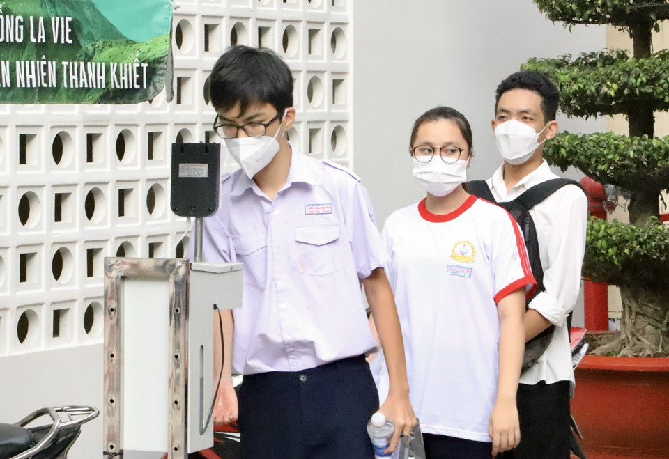 Các thí sinh kiểm tra thân nhiệt khi đến dự thi tại điểm thi trường Trung học phổ thông Bùi Thị Xuân (Quận 1). (Ảnh: Hồng Giang/TTXVN)