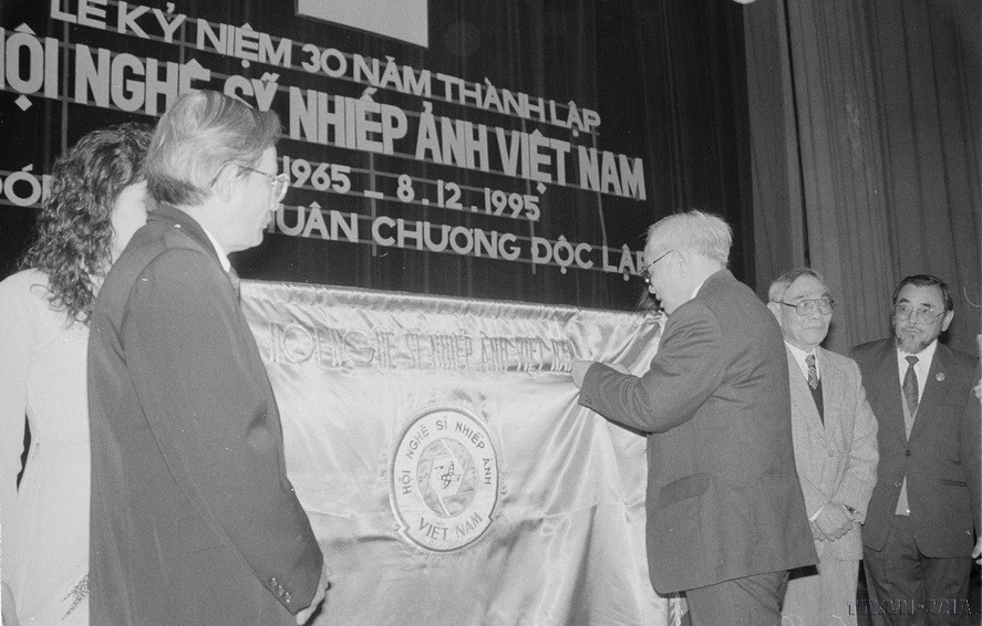 Ông Nguyễn Đức Bình, Bí thư Trung ương Đảng gắn Huân chương Độc lập lên cờ truyền thống của Hội Nghệ sỹ nhiếp ảnh Việt Nam (1995). (Ảnh: Đình Trân/TTXVN)