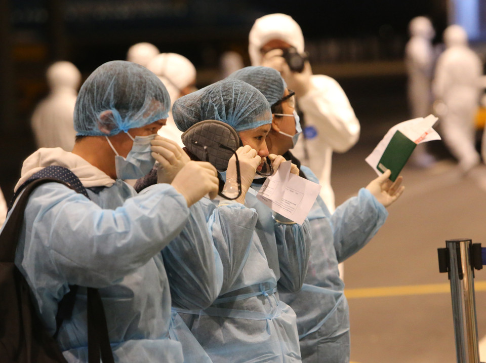 Công dân Việt Nam trở về từ Vũ Hán (Trung Quốc) được trang bị đồ bảo hộ và hướng dẫn làm thủ tục nhập cảnh tại sân bay Vân Đồn.(Ảnh: Dương Giang/TTXVN)