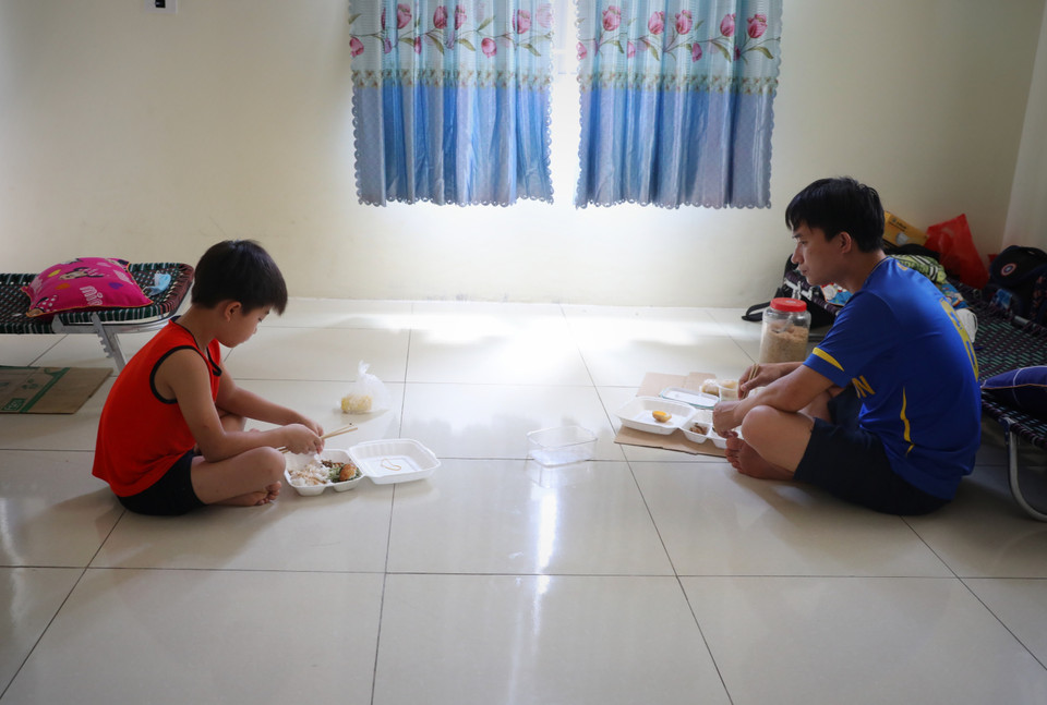 Hai bố con giữ khoảng cách trong khi ăn cơm trong khu cách ly trường Mầm non xã Việt Tiến, huyện Việt Yên. (Ảnh: Danh Lam/TTXVN)