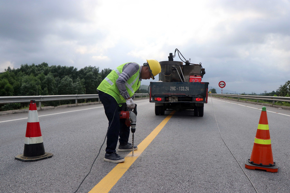 Thi công bổ sung lắp đặt các đinh phản quang giữa tim đường có hai làn xe. (Ảnh: Đỗ Trưởng/TTXVN)