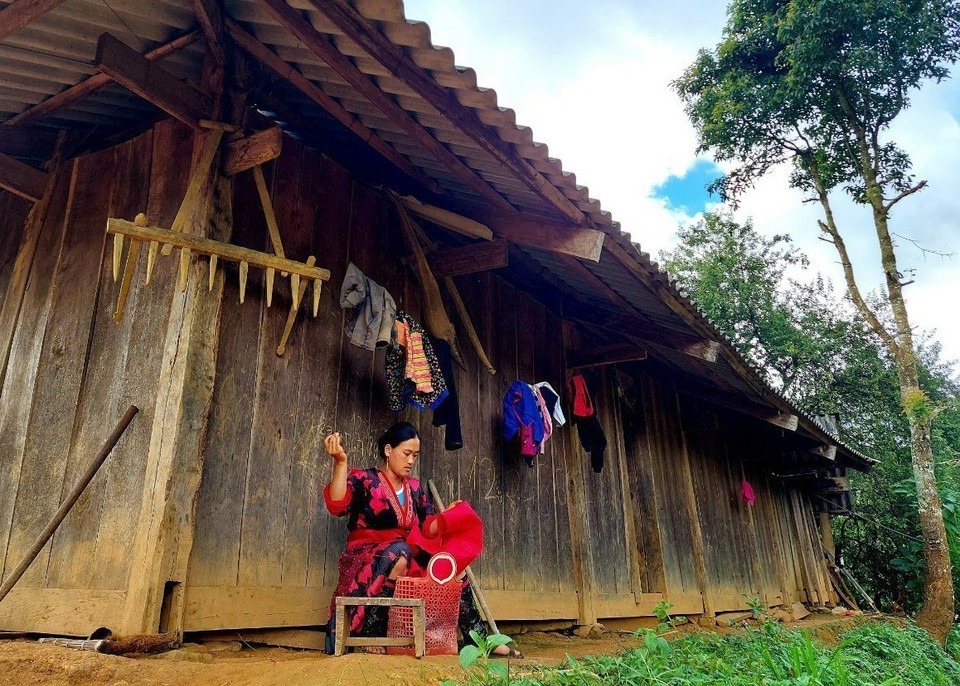 Người phụ nữ dân tộc Mông thêu thùa, may vá bên hiên căn nhà truyền thống của người Mông (ngành Mông đỏ). (Ảnh: TTXVN phát)