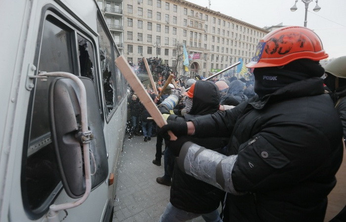 Người biểu tình dùng gậy đập phá xe buýt bên đường.