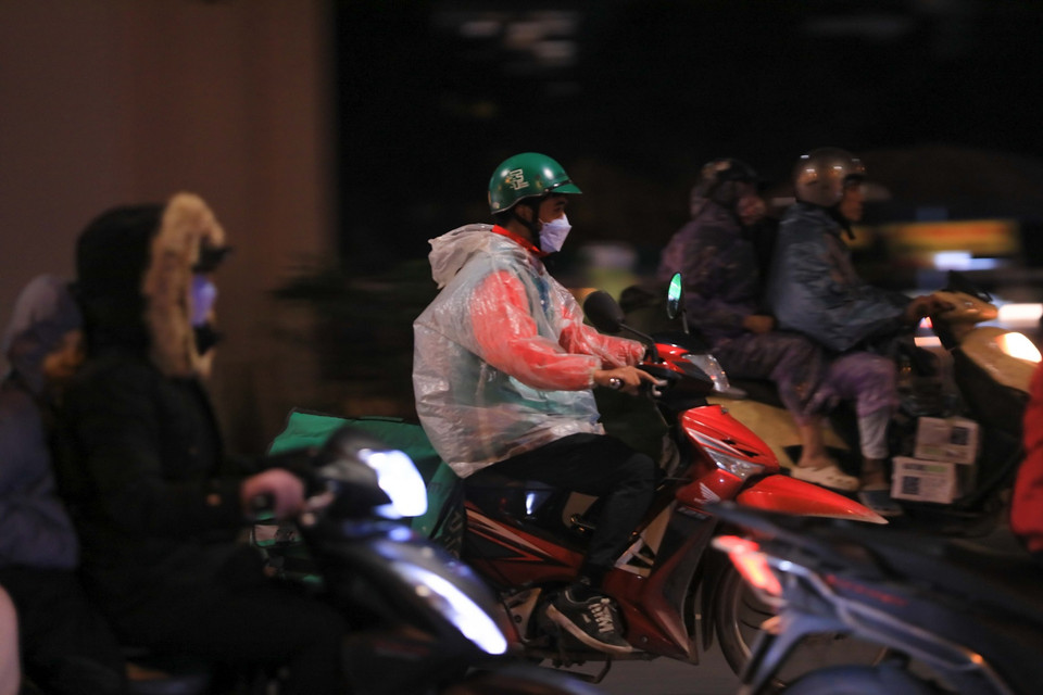 Nhiều người dân khi phải di chuyển tối 22/1 đã mặc thêm áo mưa để giữ ấm. (Ảnh: Hoàng Hiếu/TTXVN)