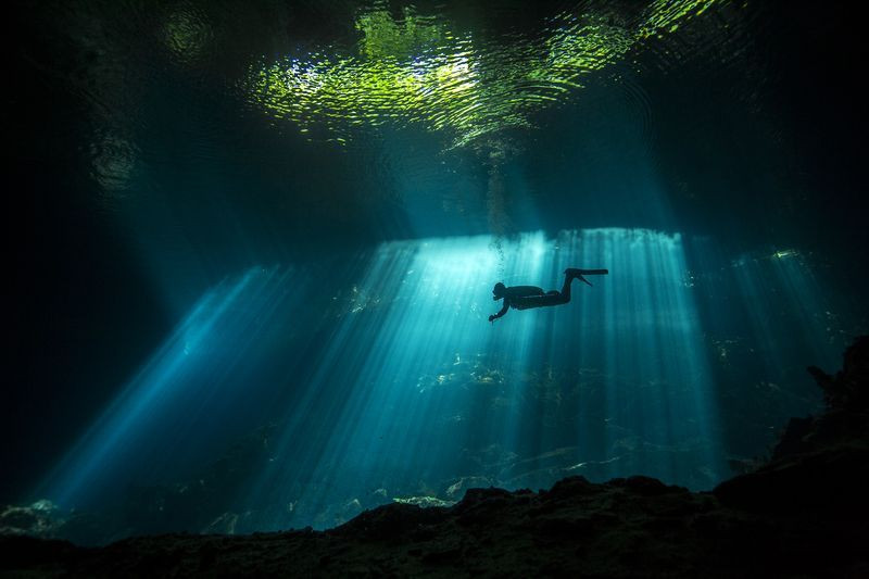 Ánh sáng mặt trời chiếu vào nước trong khi một thợ lặn bơi trong một hang động đá vôi ở Mexico, tạo nên vẻ đẹp huyền bí. (Nguồn: NatGeo)
