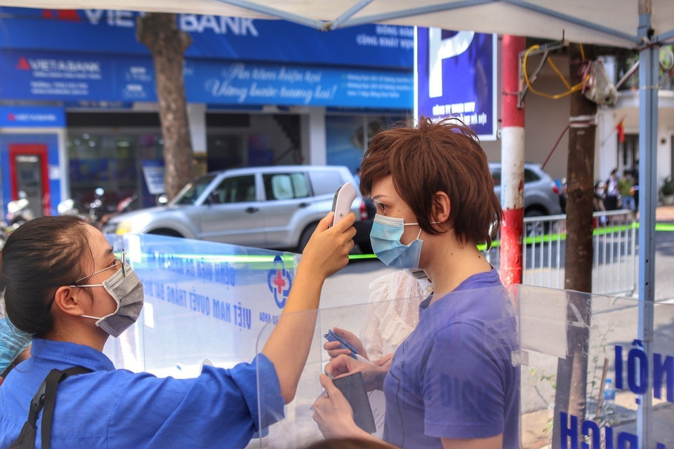 Đo thân nhiệt cho người dân đến tiêm tại điểm tiêm Bệnh viện Đa khoa Hà Nội (chiều 9/9). (Ảnh: Tuấn Đức/TTXVN)