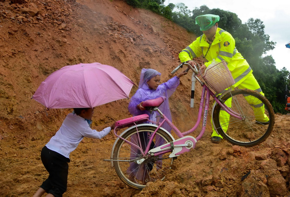 Lực lượng Cảnh sát giao thông giúp các em học sinh di chuyển qua điểm sạt lở để tới trường. (Ảnh: Xuân Tư/TTXVN)