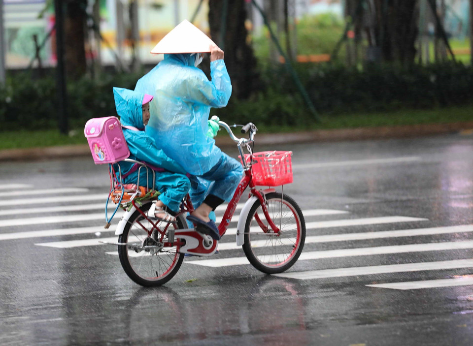 Người dân mặc áo mưa di chuyển trong cơn mưa sáng 11/8. (Ảnh: Thanh Tùng/TTXVN)