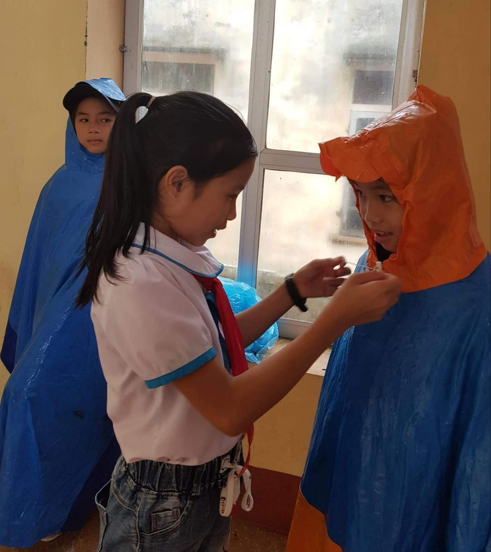 Giúp bạn mang áo mưa đi tựu trường tại Trường tiểu học Yên Lộc, huyện Can Lộc, Hà Tĩnh. (Ảnh: Phạm Thị Huế/ TTXVN)