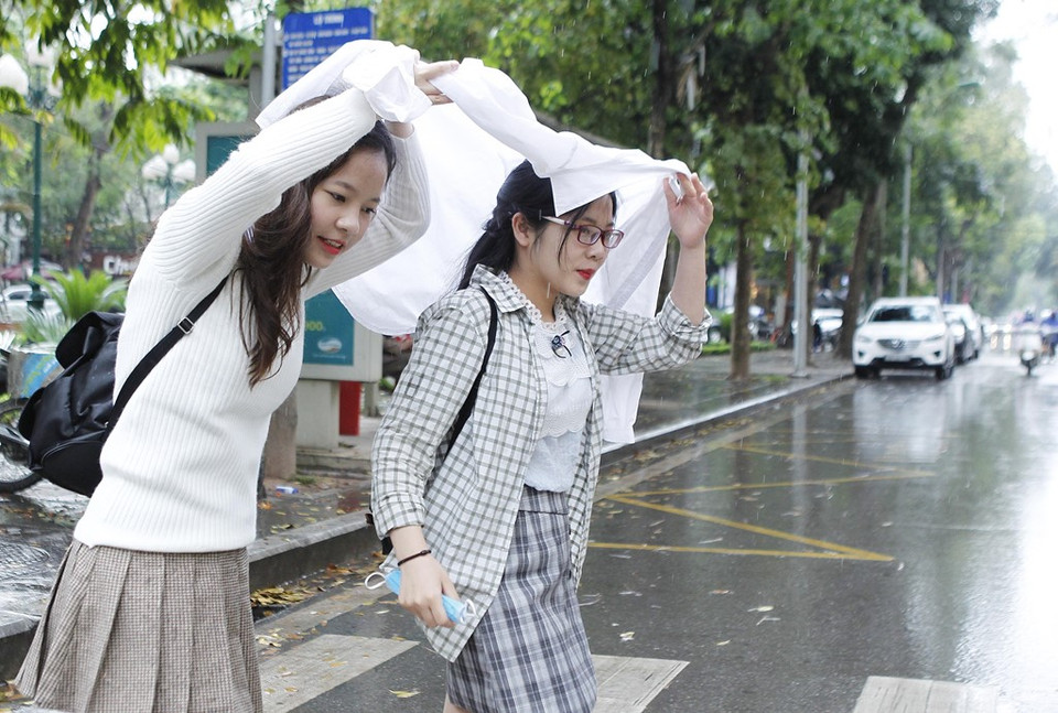 Hai sinh viên Đại học Quốc gia Hà Nội dùng áo che mưa sáng 15/4. (Ảnh: Lâm Khánh/TTXVN)
